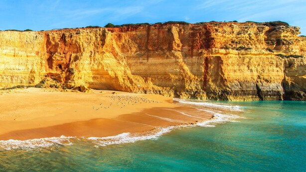 A coastal landscape with a sandy beach and cliffs.