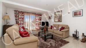 A modern living room with two beige sofas, a glass coffee table, and a large window with red and white curtains.