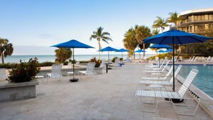 A poolside area with white lounge chairs and blue umbrellas, overlooking a beach and ocean. - Spectacular Ocean Views, Refreshing Sea Breezes with an Island Atmosphere. KW (Key West)