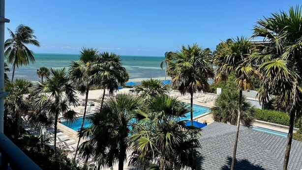 A pool area with palm trees, a beach, and a clear blue sky. - Spectacular Ocean Views, Refreshing Sea Breezes with an Island Atmosphere. KW (Key West)