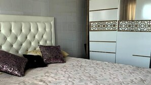 Une chambre à coucher avec une tête de lit capitonnée, une couvre-lit à motifs et une armoire ornée d’un panneau décoratif.