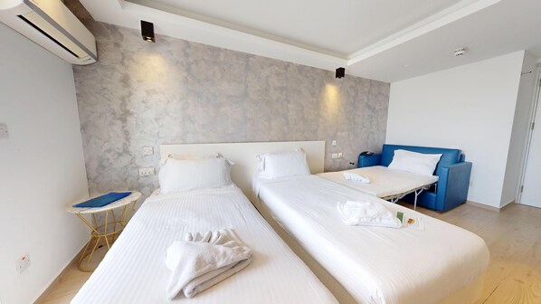 Habitación de hotel con dos camas, un sofá azul, una tabla de planchar y aire acondicionado instalado en la pared.