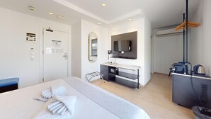 A hotel room with a bed, a desk, a mirror, a TV, and an air conditioning unit. - G Hotel by JL (St. Julian's)