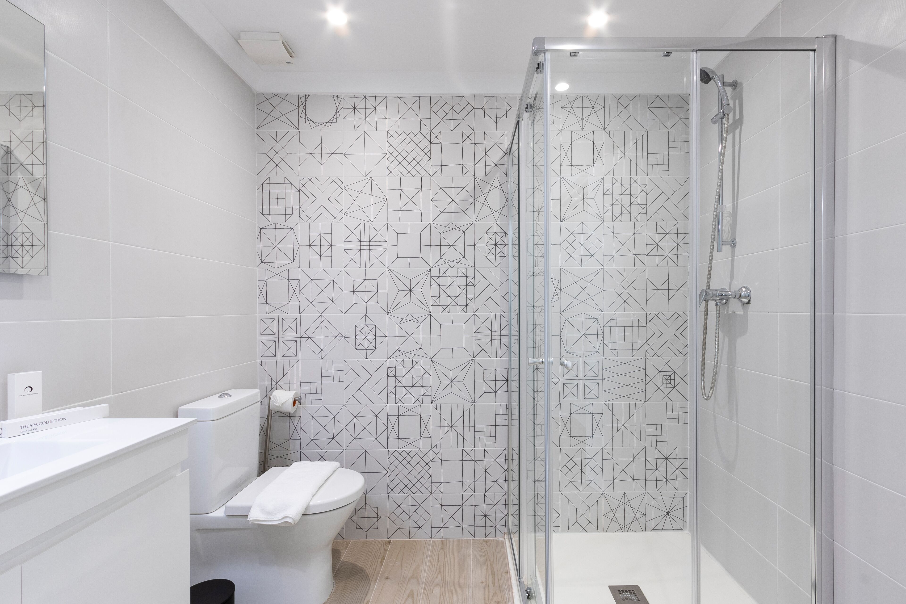 A modern bathroom with a geometric tile backsplash, a glass shower enclosure, and a white sink.
