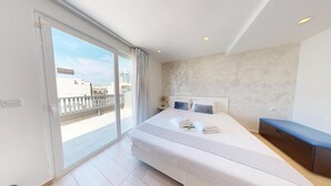A modern hotel room with a large bed, a desk, a balcony with a view of buildings, and a sliding glass door. - G Hotel by JL (St. Julian's)