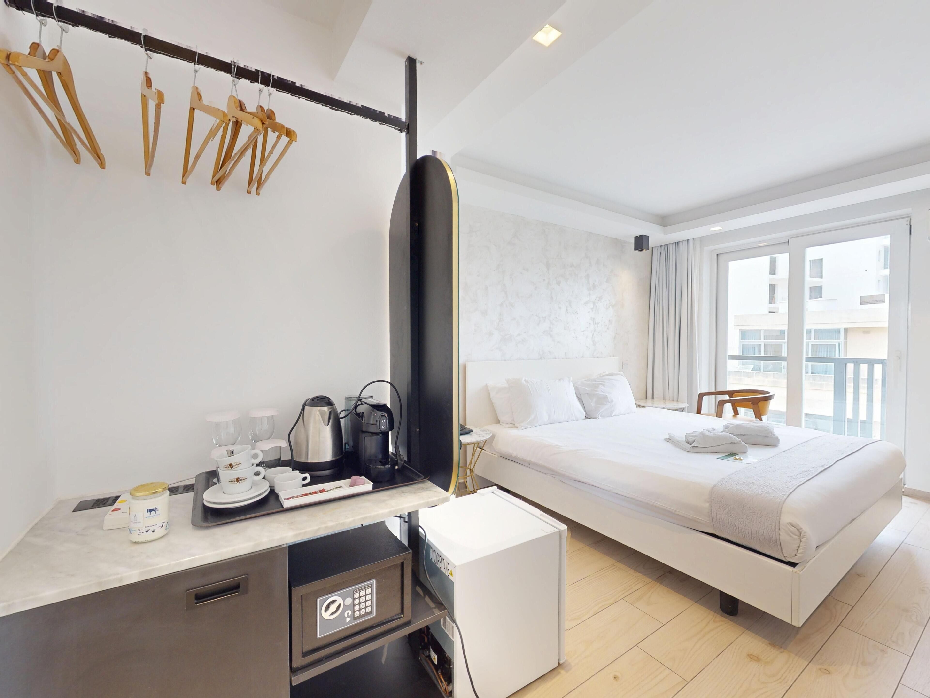 Hotelkamer met een bed, een bureau met een koffiezetapparaat, een minibar en een raam met uitzicht op gebouwen.