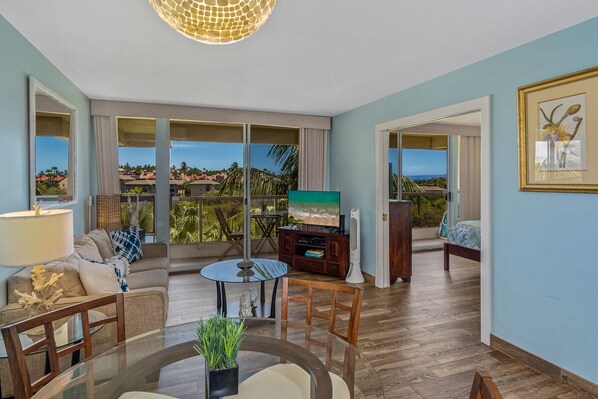 A spacious living room with a balcony, a round glass table, a sofa, and a TV.