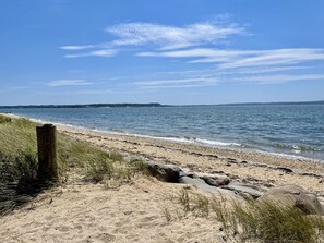 A sandy beach with a wooden post and rocks in the foreground, leading to a calm sea under a clear sky.