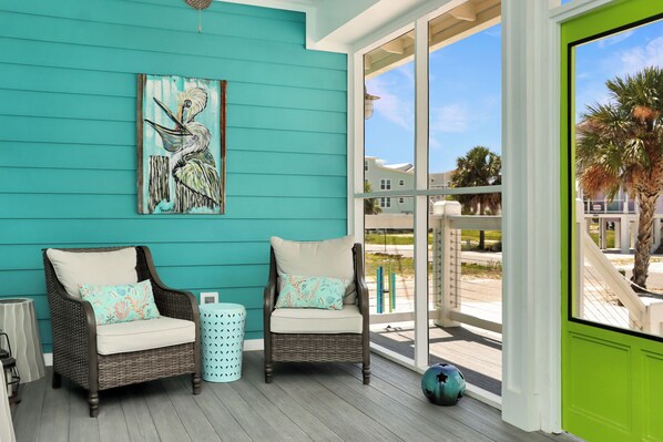 A room with teal walls, two wicker chairs with cushions, a large window, and a painting of a bird.
