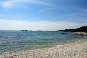 Een strand met helder water, een kiezelstrand en verre eilanden.