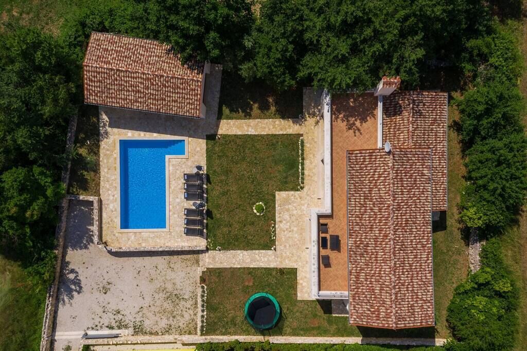 An aerial view of a property with a swimming pool, a covered patio, and a fenced yard.