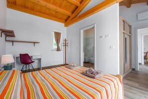 Quarto com uma cama, escrivaninha, cadeira, janela com cortinas e teto de madeira.