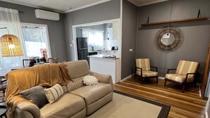 A living room with a beige sofa, two armchairs, a wooden floor, and a kitchen in the background. - Modern and Stylish 3Bed 2Bath home Townsville (Gulliver)