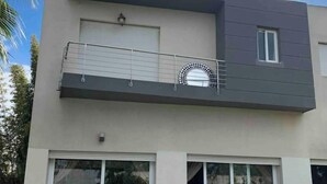 Une maison moderne à deux étages, dotée d’un balcon, de grandes portes-fenêtres coulissantes et d’un patio aménagé avec du mobilier d’extérieur.