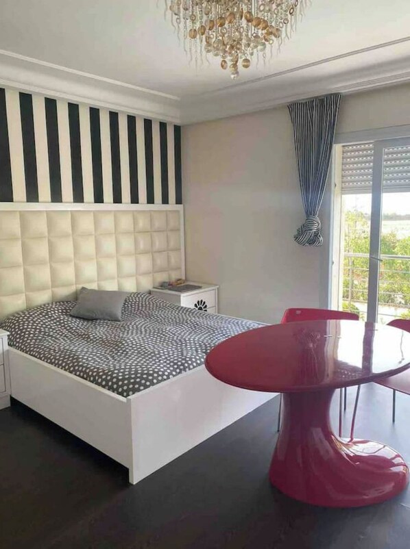Une chambre à coucher moderne avec un grand lit, une table de chevet, un fauteuil rouge et un lustre.