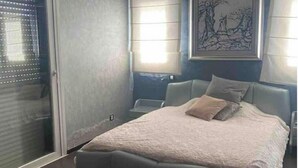 Une chambre avec un grand lit, une porte avec des stores, une lampe fixée au mur et un tableau encadré.