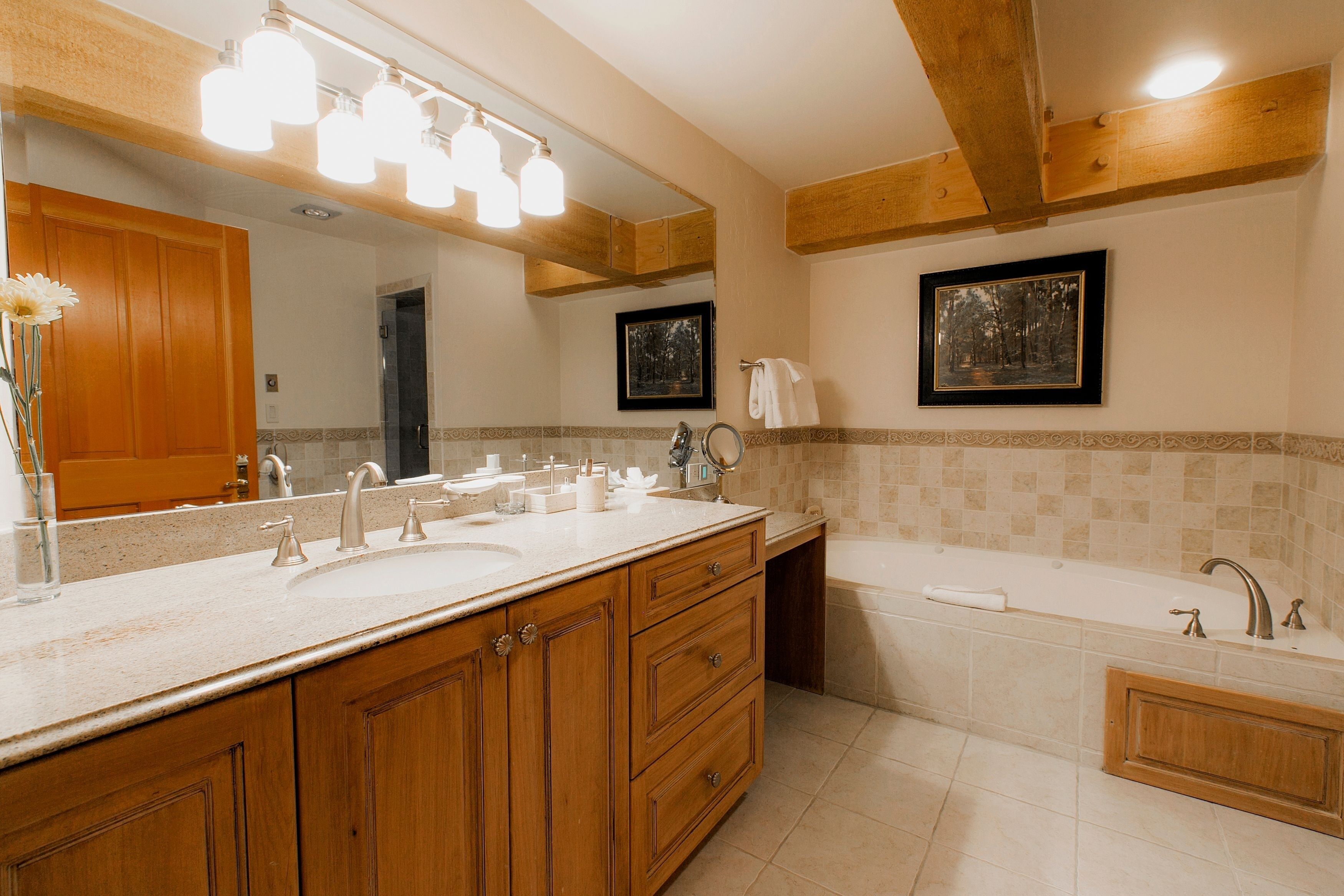 A bathroom with a wooden vanity, a large mirror, a bathtub, and two framed pictures on the wall.