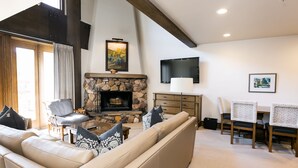 A living room with a stone fireplace, a sofa, a chair, a TV, and a table with chairs.