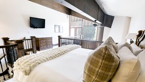 A bedroom with a large bed, a wooden headboard, a TV mounted on the wall, and a balcony with a view of the outdoors.