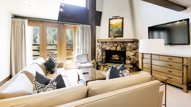 A living room with a stone fireplace, a sofa set, a television, and a large window with curtains.