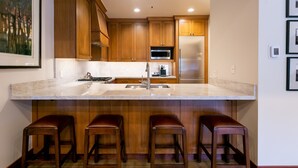 A kitchen with wooden cabinets, a stainless steel refrigerator, a microwave, and a large island with a sink and bar stools. - Luxury Four Bedroom Multi-Level Townhouse 4 Townhouse by RedAwning (Park City)