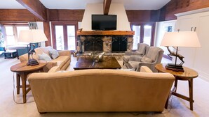 A cozy living room with a stone fireplace, wooden beams, and a flat-screen TV mounted above it. There are two sofas and two side tables with lamps. - Luxury Four Bedroom Multi-Level Townhouse 4 Townhouse by RedAwning (Park City)