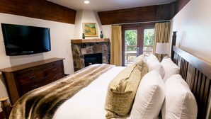 A bedroom with a large bed, a flat-screen TV, a stone fireplace, and a balcony with curtains. - Luxury Four Bedroom Multi-Level Townhouse 4 Townhouse by RedAwning (Park City)