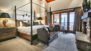 A four-poster bed with a wooden headboard, a sofa, a fireplace, and a television mounted on the wall.