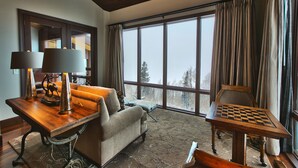 A cozy room with a large window, a wooden table with a chessboard, a sofa, and a lamp.