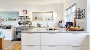 A modern kitchen with white cabinetry, a central island, and a window with decorative metalwork. - Coastal - Wittering  -  an annexe that sleeps 6 guests  in 3 bedrooms (West Wittering)