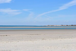Een breed zandstrand met een heldere blauwe lucht en een rustige zee.