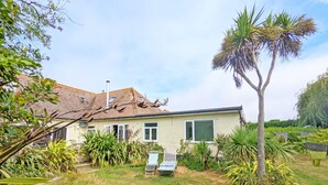 A house with a tiled roof, a lawn, and various plants including a palm tree. - Coastal - Wittering  -  an annexe that sleeps 6 guests  in 3 bedrooms (West Wittering)