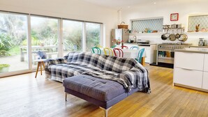 A modern living room with a sofa, a dining table with colorful chairs, and a kitchen area with a stove and cabinets. - Coastal - Wittering  -  an annexe that sleeps 6 guests  in 3 bedrooms (West Wittering)