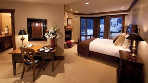 A hotel room with a bed, desk, chair, and a fireplace.