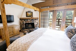 A bedroom with a stone fireplace, wooden beams, a bed, a TV, and a view of the outdoors. - Main Lodge Luxury King Room With Hot Tub Hotel Room by RedAwning (Park City)