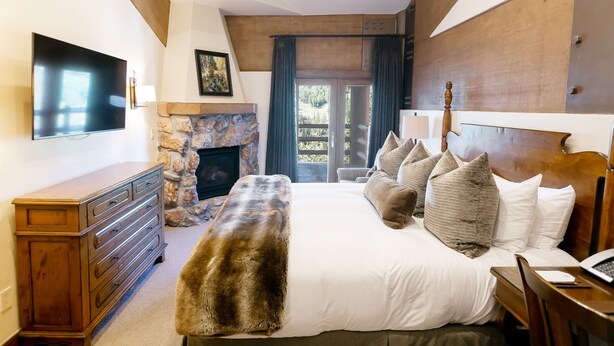 A bedroom with a stone fireplace, a large bed with multiple pillows, a dresser, and a television on the wall. - Luxury One Bedroom with Mountain View 1 Apartment Hotel by RedAwning (Park City)