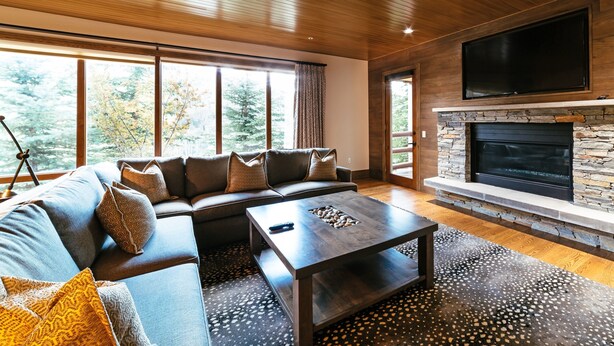 A modern living room with a stone fireplace, a large flat-screen TV, and a sectional sofa with patterned cushions. - Luxury One Bedroom Corner Suite 1 Apartment Hotel by RedAwning (Park City)