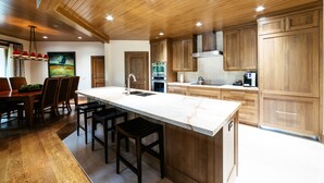 A modern kitchen with wooden cabinets, a marble island, and a dining area with a table and chairs. - Luxury One Bedroom Corner Suite 1 Apartment Hotel by RedAwning (Park City)