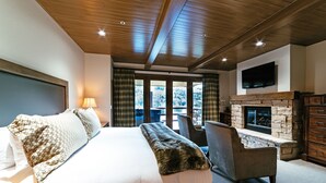 A bedroom with a large bed, a stone fireplace, a television, and a view of the outdoors. - Luxury One Bedroom Corner Suite 1 Apartment Hotel by RedAwning (Park City)