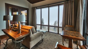 A cozy living room with a large window, a wooden table, a sofa, and a chess table.