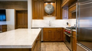 A modern kitchen with wooden cabinets, a marble countertop, a stainless steel refrigerator, and a built-in oven.