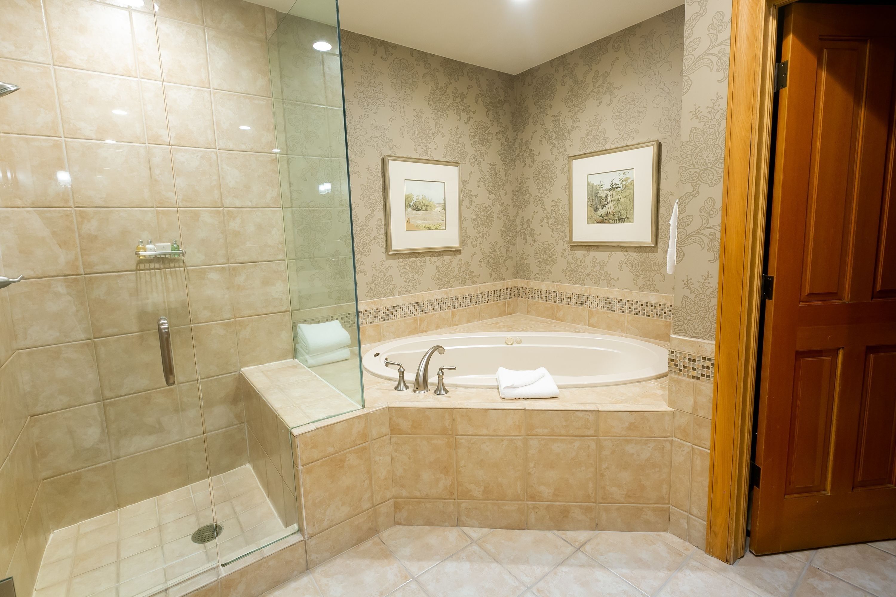 Un baño con ducha de vidrio, bañera independiente y dos cuadros en la pared.