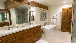 Ein modernes Badezimmer mit großem Spiegel, zwei Waschbecken, einer Badewanne, Holzschränken und einer Duschkabine.