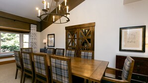 A dining room with a wooden table and chairs, a chandelier, and a large window with a view of trees. - Luxury Four Bedroom Multi-Level Townhouse with Hot Tub 4 Townhouse by RedAwning (Park City)