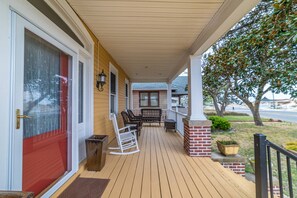 A wooden porch with a red door, a brick column, and a seating area with chairs and a table.