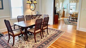 A dining room with a wooden table and chairs, a chandelier, and a floral rug. - Beachfront Home with Sunset Views, Steps to Bay (Cape Charles)