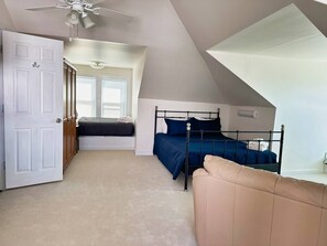 A bedroom with a sloped ceiling, a bed with a metal frame, a beige sofa, and a door leading to another room.