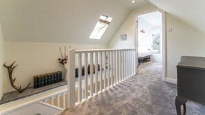 Un dormitorio amplio en el ático, con techo inclinado, tragaluz, barandilla blanca y vista a una habitación contigua.