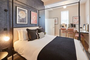 A modern bedroom with a large bed, bedside tables, and a vanity area with mirrors and a sink.