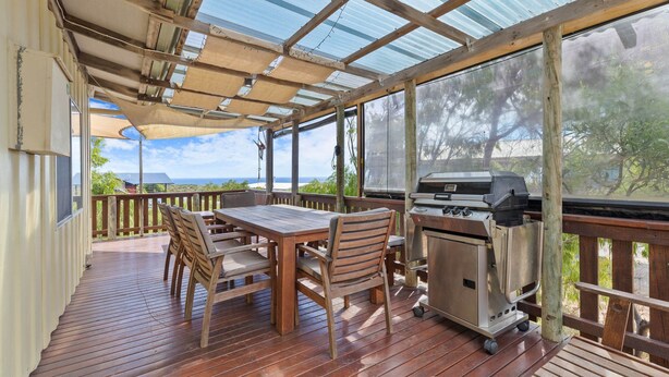 En takförsedd uteplats med en grill, trädgårdsmöbler och utsikt över havet.